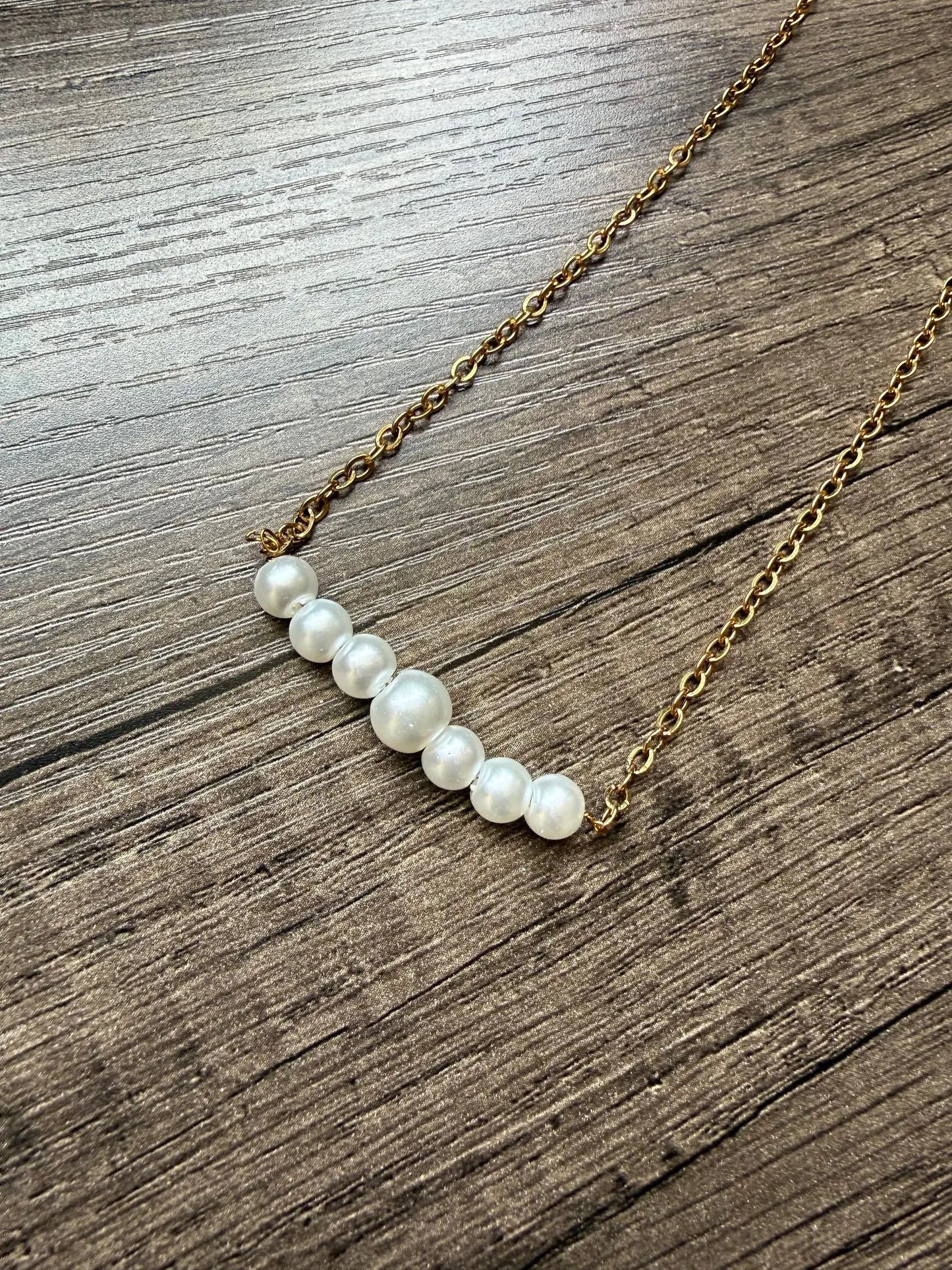 Pearl necklace on a gold chain lying on a wooden surface