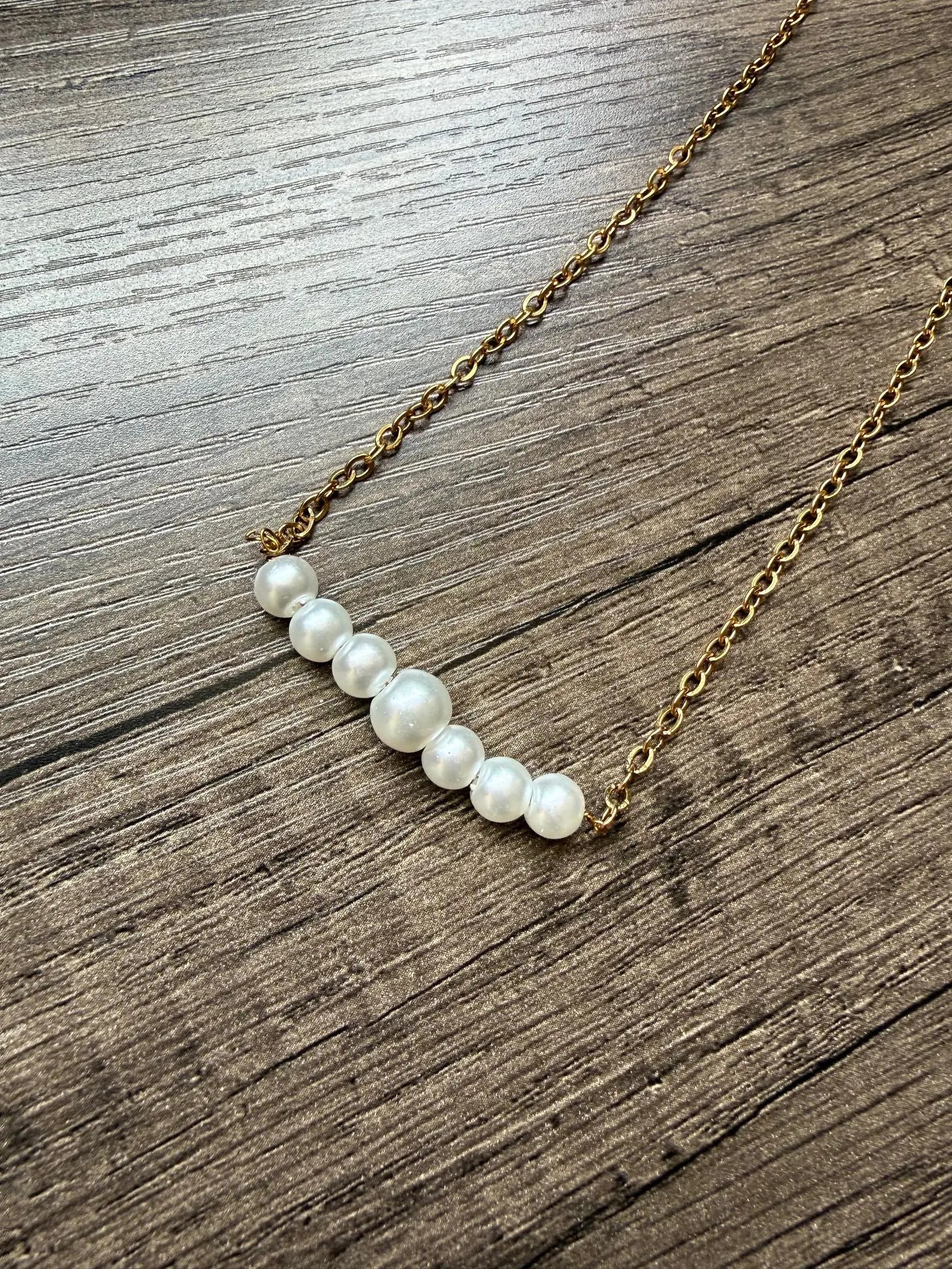 Pearl necklace on a gold chain lying on a wooden surface